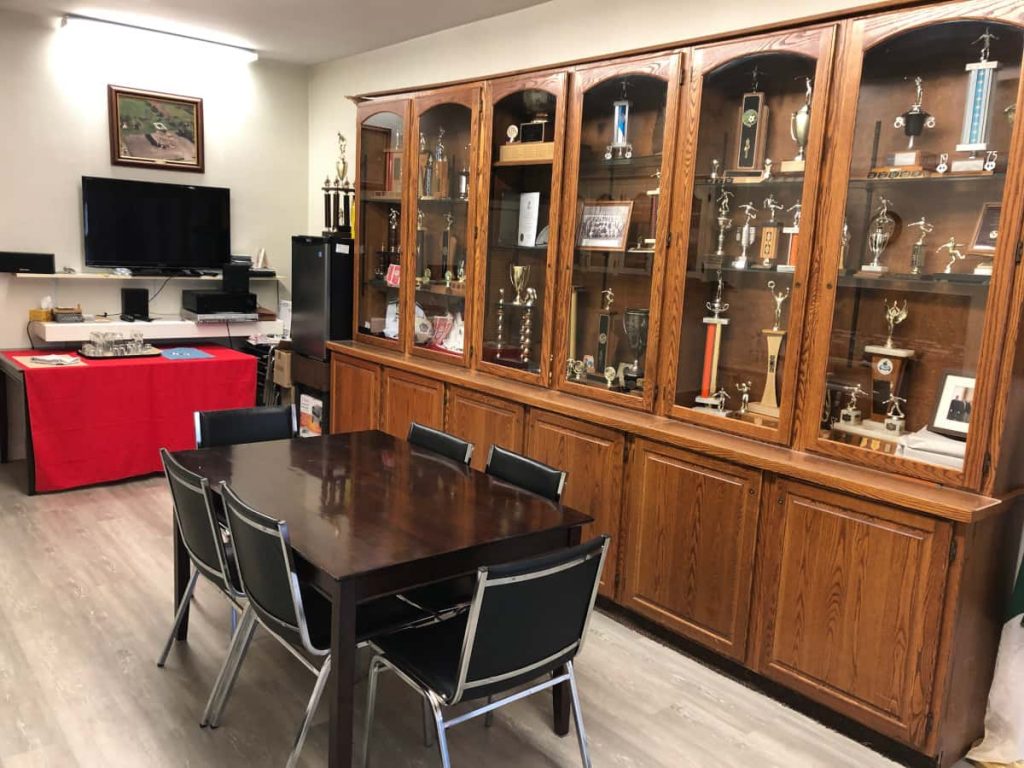 Interior view of our new premises on Franklin, showing a table with 6 chairs, sink, trophy case with all its trophies and TV and mini-fridge